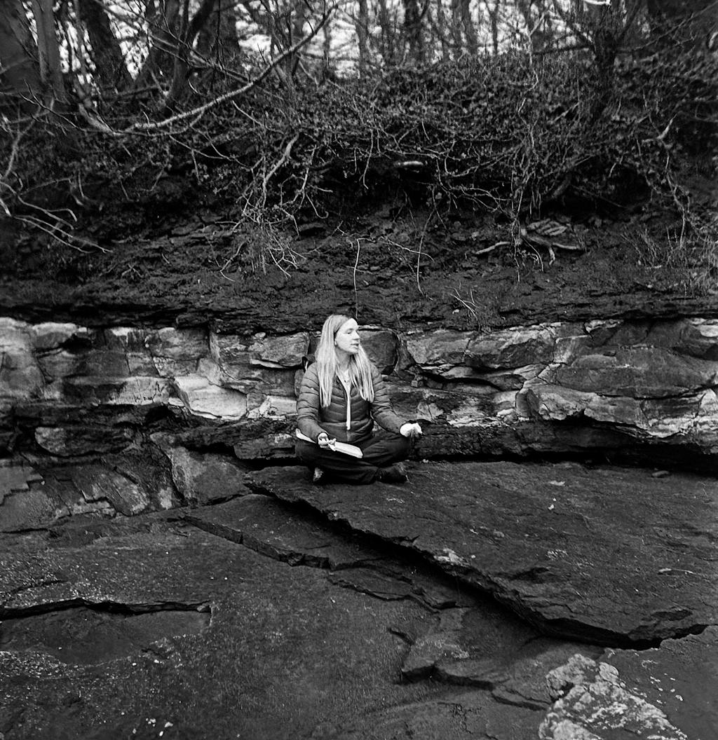 Black and white photo of woman meditating in a nature setting, surrounded by slate and trees. Captured by Anthony Robson on Fomapan Creative 200 - 120 Film.