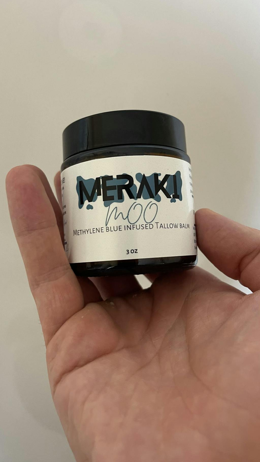 Hand holding a jar of Meraki methylene blue infused tallow balm.