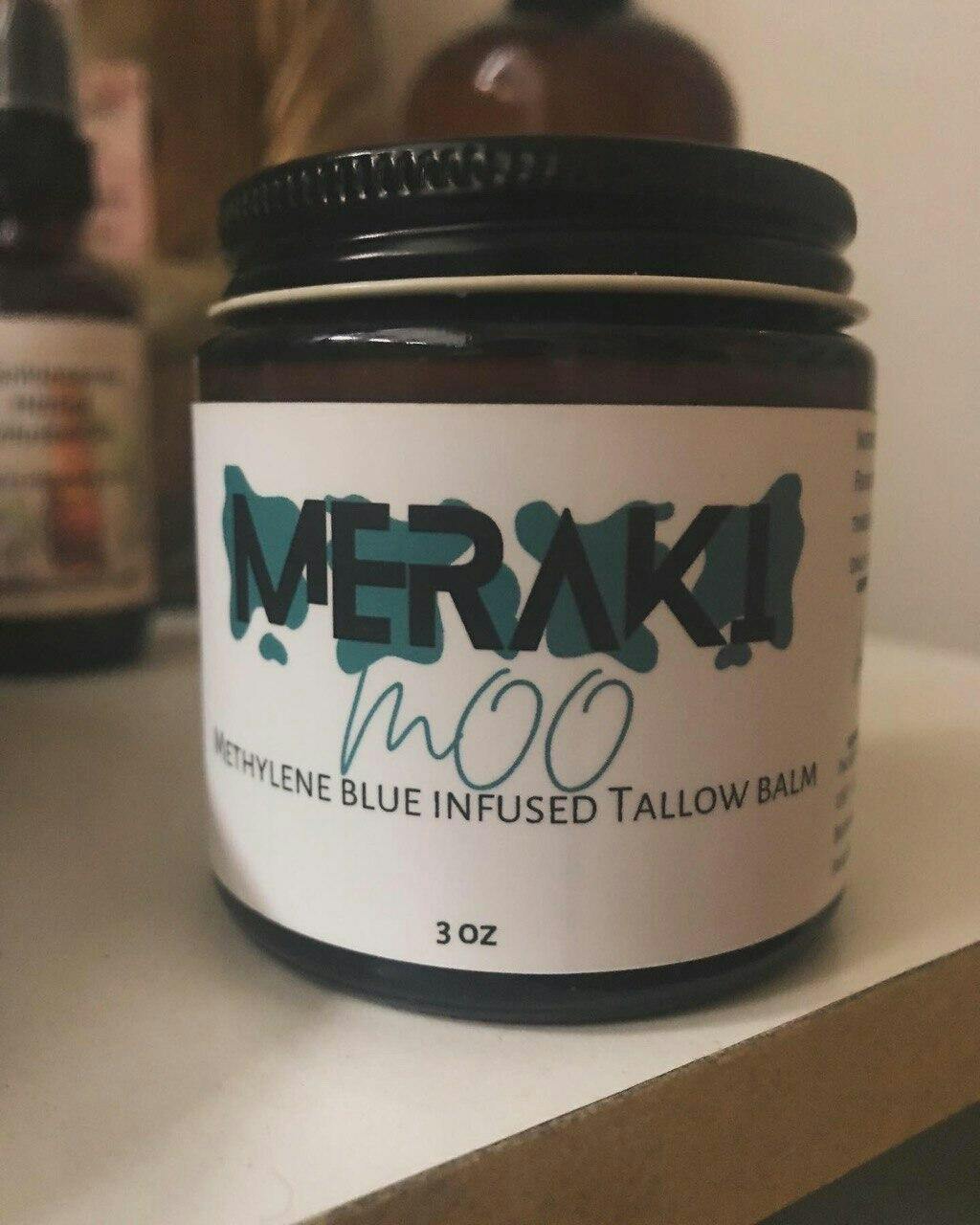 Jar labeled 'Meraki MOO Methylene Blue Infused Tallow Balm,' placed on a shelf.