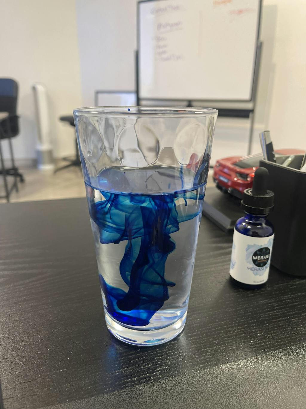 Glass of water with blue ink swirling inside on a desk.