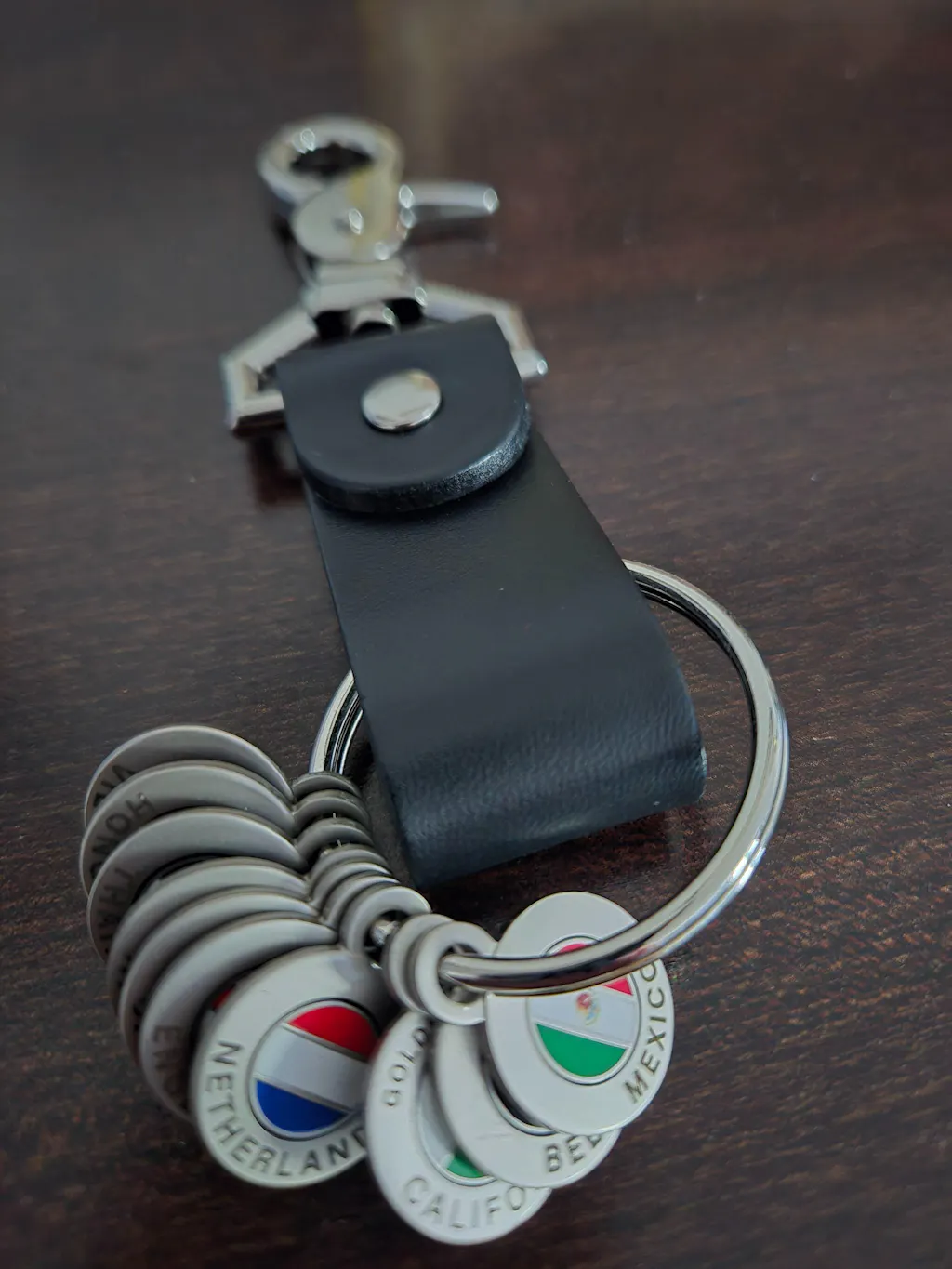 Close-up of a Black Wanderchain leather keychain holding country Tokens including Netherlands and Mexico